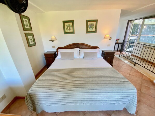 A neatly made bed with white linens and a striped blanket, two bedside tables with lamps, framed pictures on the wall, and a balcony with a railing. - Spacious house in Resort. (Taormina)