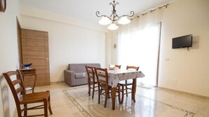 Un coin repas avec une table et des chaises, un canapé, un téléviseur fixé au mur et une porte en bois.