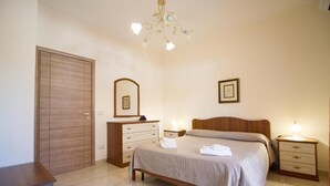 Une chambre à coucher avec une armoire en bois, une table de chevet avec une lampe, un lit avec une tête de lit et un miroir au mur.