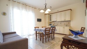 Un salon comprenant un canapé, une table à manger avec des chaises, un coin cuisine avec des placards et des appareils électroménagers, et un bol bleu décoratif posé sur une table.