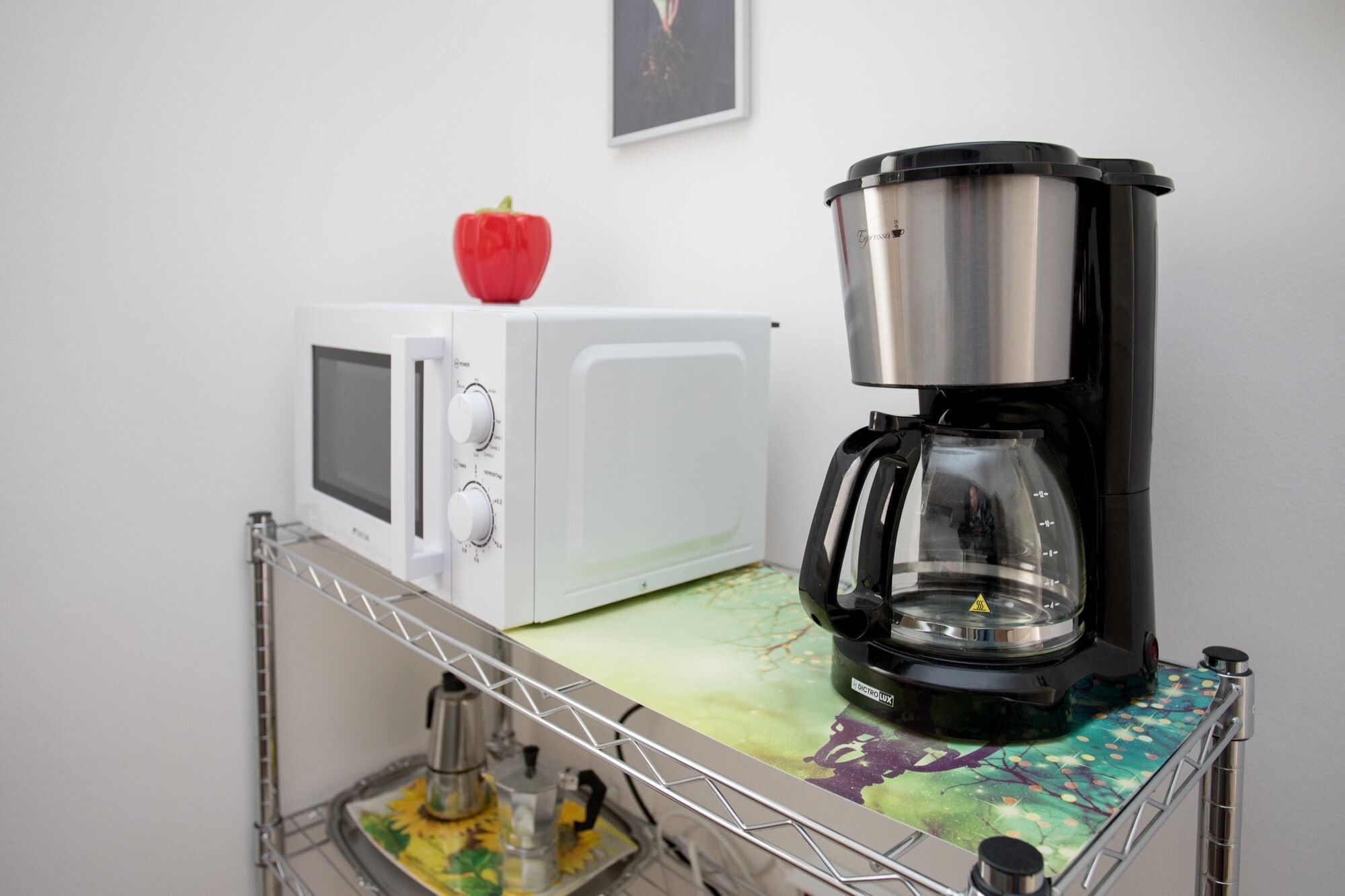 Une petite cuisine équipée d’un four à micro-ondes, d’une machine à café et d’une petite pomme rouge posée sur le four à micro-ondes.
