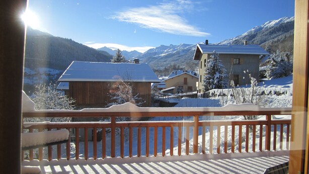 Une terrasse en bois offrant une vue sur des maisons et des montagnes enneigées.