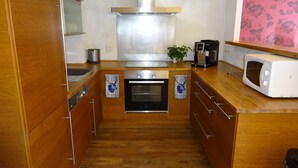 Une cuisine compacte dotée de meubles en bois, d’un four encastré, d’un four à micro-ondes et d’une machine à café.