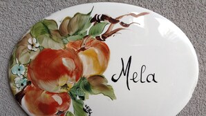 Un objet blanc de forme ovale, orné d’un motif floral et portant l’inscription « Mela ».