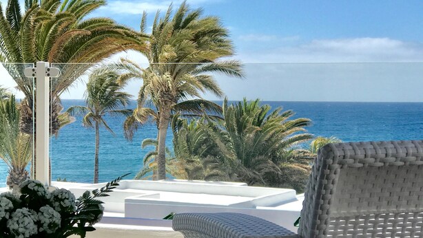 Een rieten stoel en tafel met uitzicht op de oceaan en palmbomen.