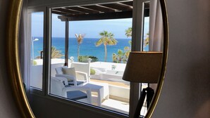 Een ronde spiegel toont een balkon met witte lounge fauteuils, een lamp en uitzicht op zee.