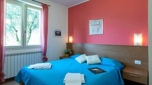 Een slaapkamer met een blauw beddekleed, een houten hoofdbord, een nachtkastje met een lamp en een raam met roze gordijnen.