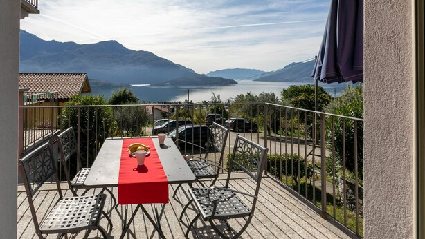 Een balkon met een tafel en stoelen, met uitzicht op een meer en bergen.