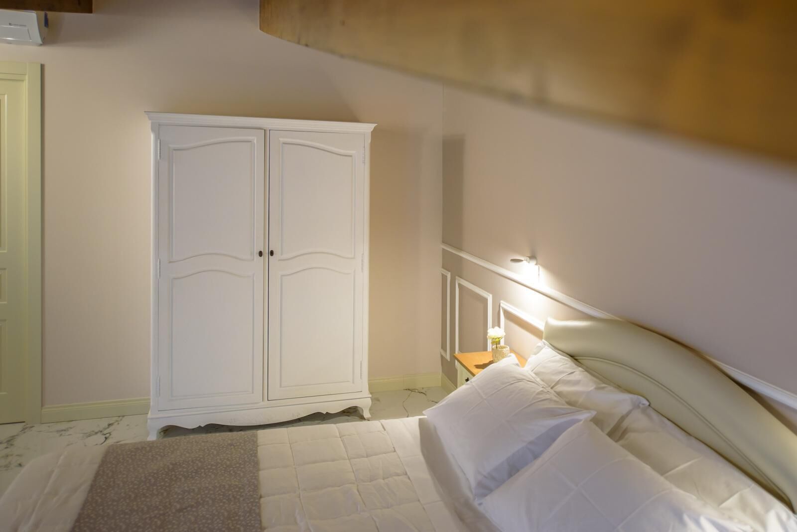 A bedroom with a bed, white wardrobe, and a nightstand with a lamp.