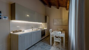 A modern kitchen with a marble floor, white cabinetry, and a dining area with a table and chairs. - Apartment Standard Suite  4 (Vasto)
