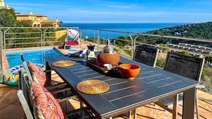 A terrace with a pool, dining table, and chairs overlooking a scenic view of the sea and hills. - Villa with stunning sea views and pool in terrace. (Sa Riera)