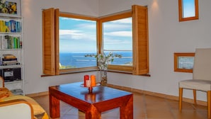 A room with a large window offering a view of the sea, a wooden table, a bookshelf, and a chair. - Villa with stunning sea views and pool in terrace. (Sa Riera)