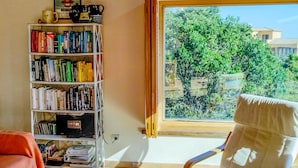 A room with a large window, a bookshelf, a chair, and a table with a candle. - Villa with stunning sea views and pool in terrace. (Sa Riera)