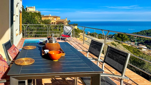 A sunlit outdoor dining area with a pool, a table with chairs, and a view of the sea. - Villa with stunning sea views and pool in terrace. (Sa Riera)