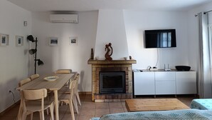 Una sala de estar moderna con chimenea, mesa de comedor y sillas. Hay un televisor montado en la pared y una lámpara en el techo.