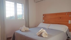 Una cama bien hecha con un edredón acolchado, dos almohadas y dos toallas enrolladas.