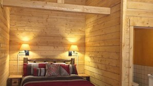 Ein Holzhüttenraum mit einem Bett, zwei Nachttischlampen und einem sichtbaren Badezimmer mit Toilette und Waschbecken.