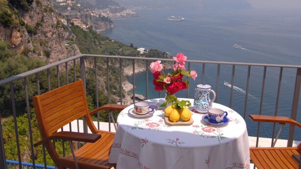 A balcony with a table set for two, overlooking a coastal landscape with a ship in the distance. - CONCA "Marechiaro" AMALFI COAST (Conca dei Marini)