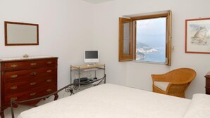 A bedroom with a bed, a dresser, a desk with a computer, a chair, and a window with a view of the sea. - CONCA "Marechiaro" AMALFI COAST (Conca dei Marini)