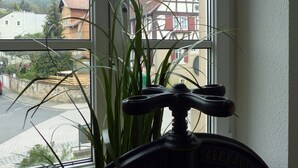 Ein Fenster mit Blick auf eine Straße und Gebäude, eine Topfpflanze und ein Wasserhahn.