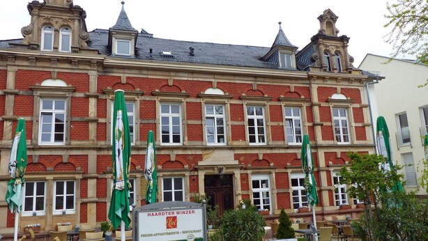 Ein historisches Gebäude mit einem Schild für 'Haardter Winzer', das es als Restaurant und Apartments kennzeichnet.