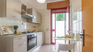 Une cuisine moderne équipée d’une cuisinière à gaz, d’un four et d’une hotte en acier inoxydable. On y trouve également un coin repas avec une chaise blanche et une table.