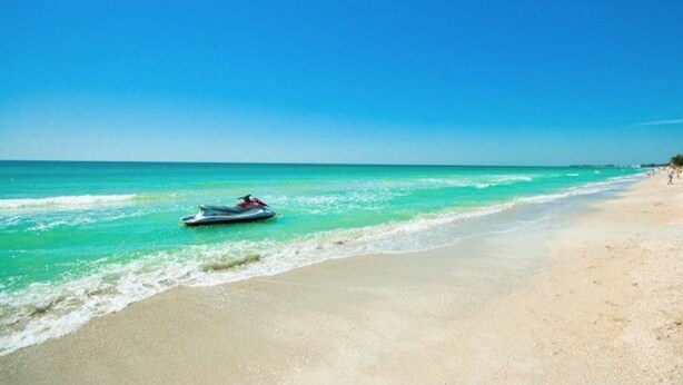 Una playa con un jet ski en el agua y una orilla arenosa.