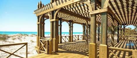 Un pabellón de madera en la playa con techo a cuadros y paredes abiertas, con vista al mar.