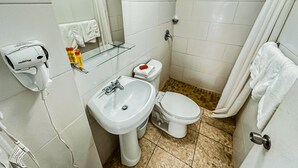 A bathroom with a white sink, toilet, and shower. There is a glass shelf above the sink and a towel rack on the wall. - Loft Aparment Steps From Nightlife, Gladiolas II /Loft + Room /Free WIFI - 2101 (Ponce Pueblo)