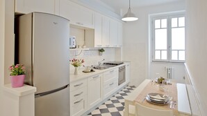 A modern kitchen with white cabinets, a stainless steel refrigerator, a dining table set for two, and a window providing natural light.