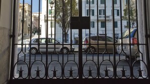 A wrought iron gate with intricate designs, leading to a building with multiple windows and balconies.
