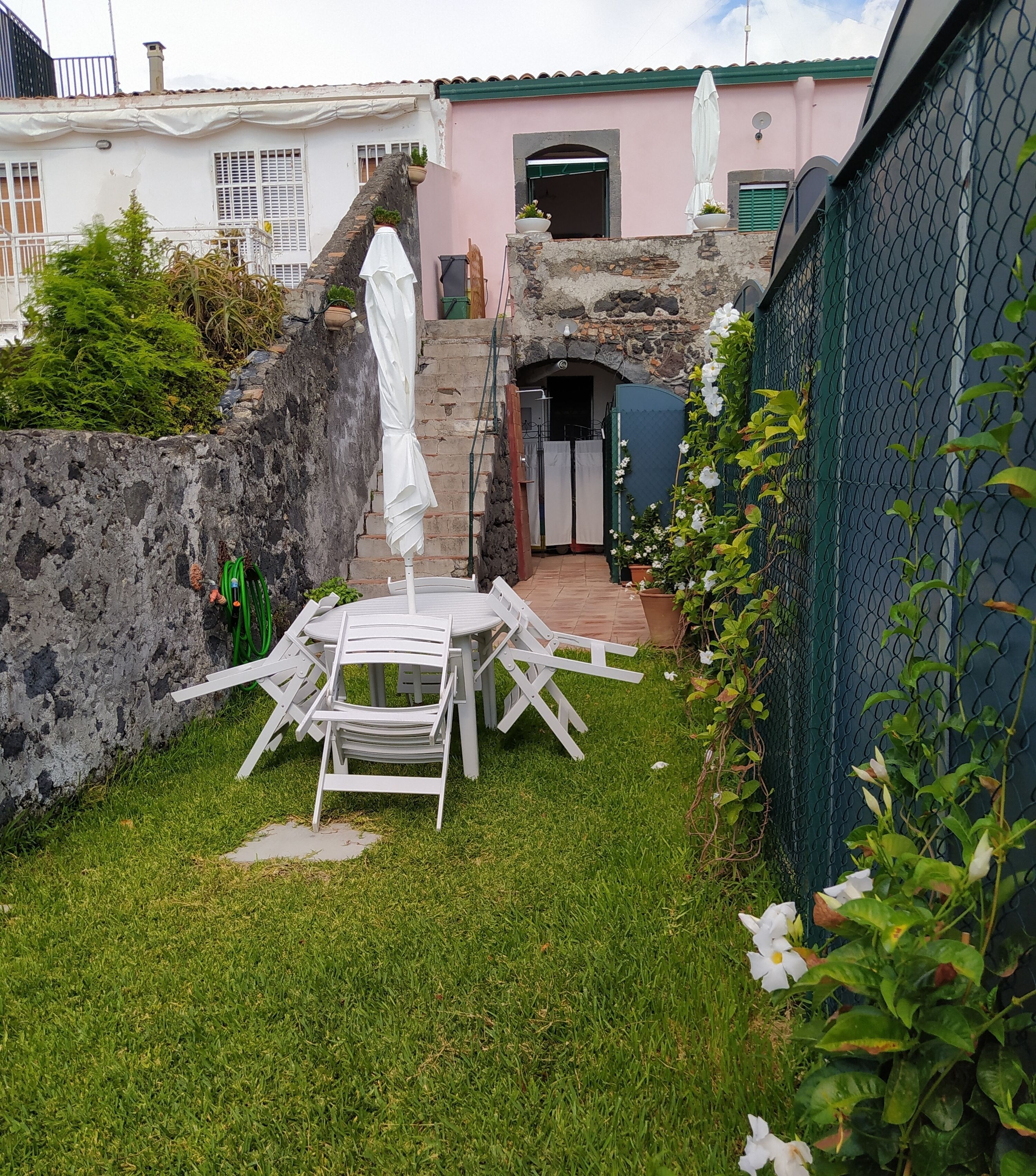 Un pequeño patio al aire libre con una mesa y sillas, rodeado por un muro de piedra y una valla.