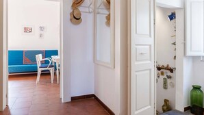 Un couloir avec un canapé bleu, des chaises blanches et une porte ornée de chapeaux et d’objets décoratifs.