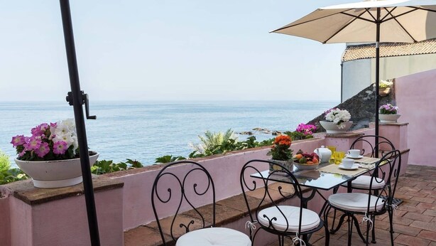 Une terrasse avec une table et des chaises, un pot de fleurs et une vue sur la mer.