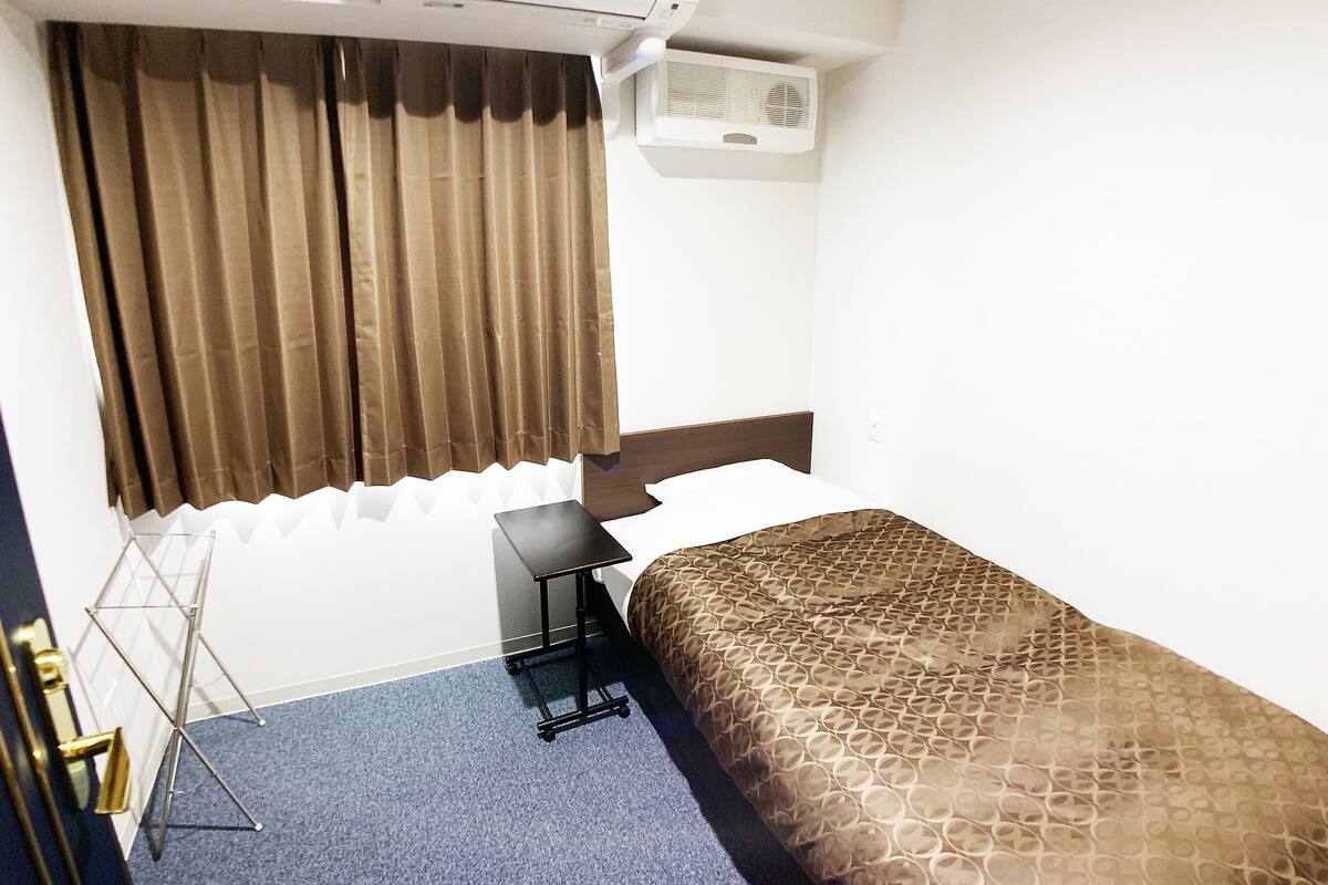 Een hotelkamer met een bed, een bureau, een airconditioning en een raam met gordijnen.