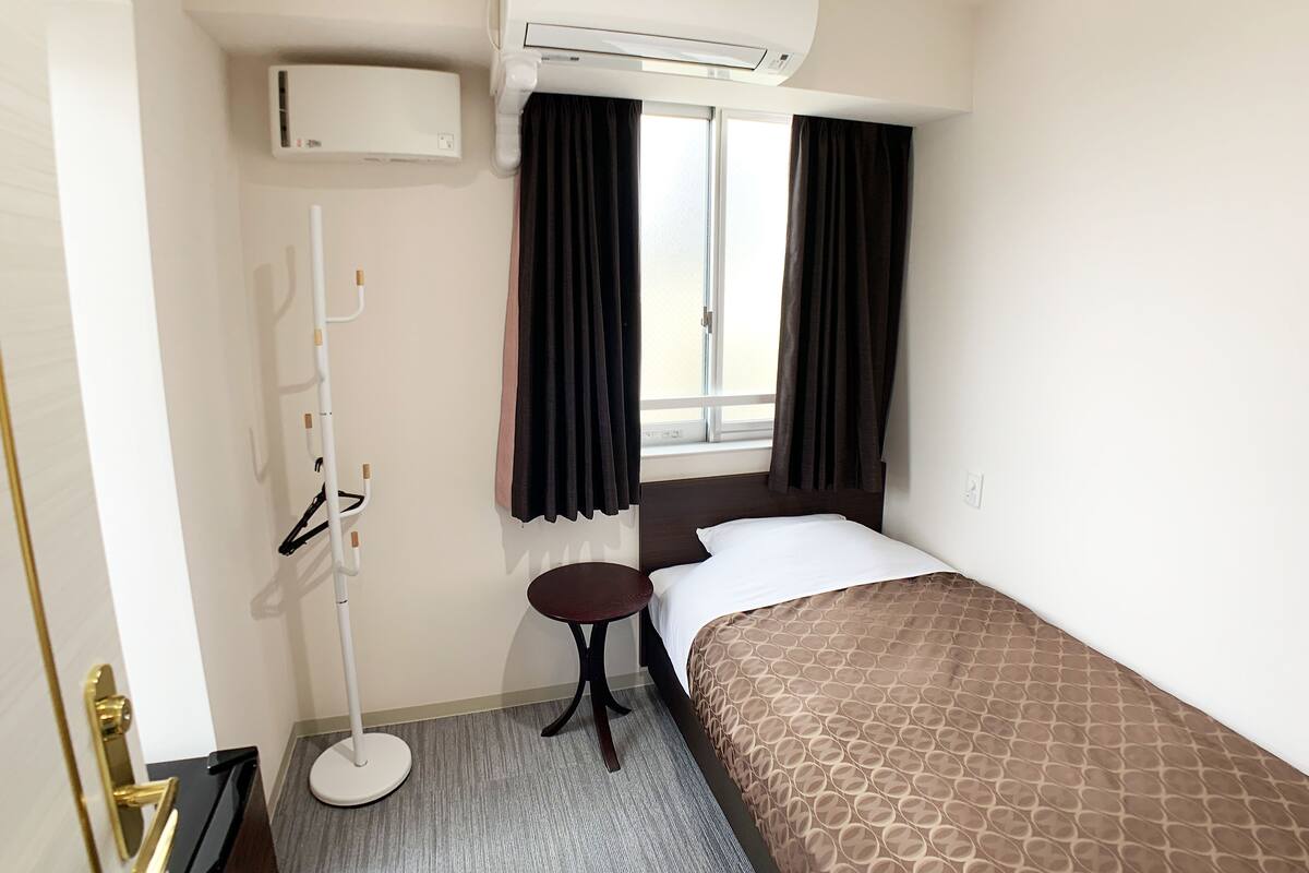 Een hotelkamer met een bed, een elektrische kachel, een airconditioner en een raam met gordijnen.
