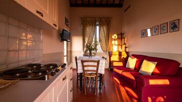 Un salon confortable avec un canapé rouge, une table à manger avec des chaises, une cuisine équipée d’une cuisinière et un téléviseur fixé au mur.