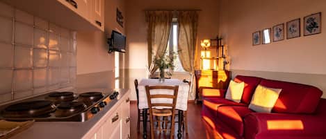 Un salon confortable avec un canapé rouge, une table à manger avec des chaises, une cuisine équipée d’une cuisinière et un téléviseur fixé au mur.
