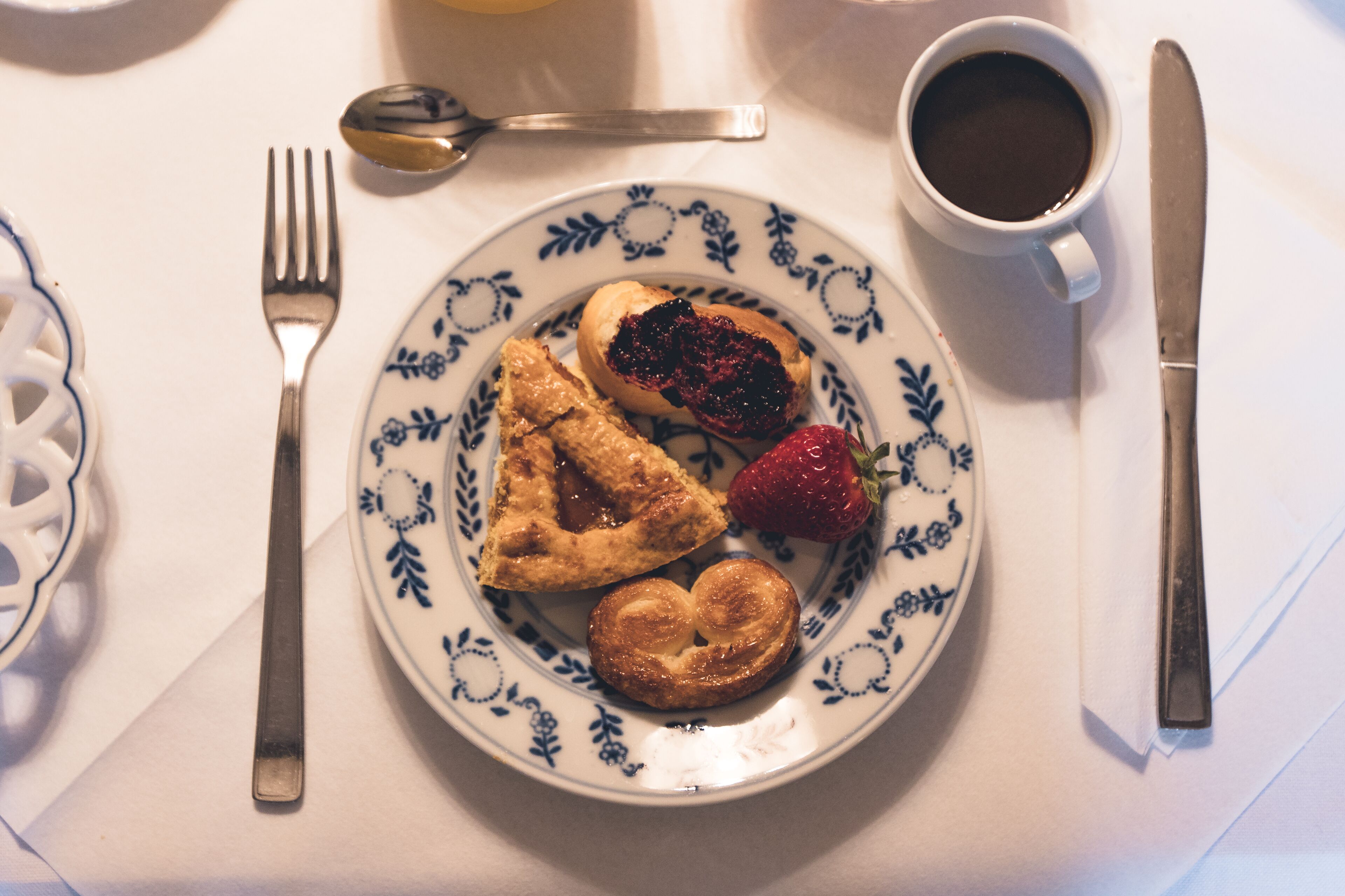 A plate with pastries and a strawberry, a cup of coffee, and cutlery on a table.