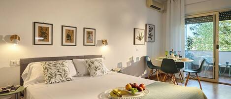 A hotel room with a bed, a dining table with chairs, and a balcony with a view.