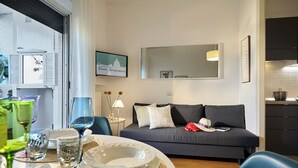 En moderne stue med en grå sofa, et spisebord med tallerkener og glas, og et køkkenområde i baggrunden.
