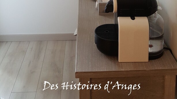 Une pièce avec une table en bois, une lampe, une machine à café et une affiche au mur.
