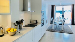 A modern kitchen with a built-in oven, a toaster, and a sink. There is a dining area with a table and chairs, and a view of the outside through a large window. - Luxurious Penthouse (Atico) ‘La Mar Altea', max. 4p (Altea)