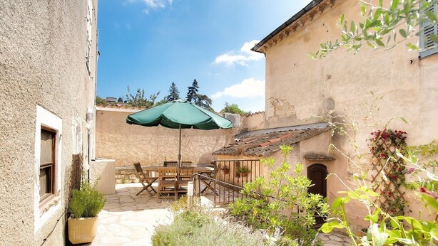 A courtyard with a wooden table and chairs, an umbrella, and potted plants. - THE GARDEN OF THE VILLAGE IN VALBONNE (3 ***): live in-out (Valbonne)