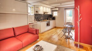 A compact living space with a red sofa, a dining table with chairs, a kitchen area with a stove and oven, and a red accent wall. - THE GARDEN OF THE VILLAGE IN VALBONNE (3 ***): live in-out (Valbonne)