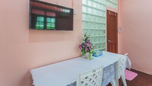 Una habitación con una televisión instalada en la pared, una mesa con mantel de encaje, un jarrón con flores y una puerta con ventana.