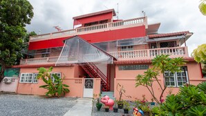 Un edificio de varios pisos con fachada roja y rosa, una escalera visible, y plantas en macetas en primer plano.