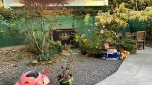 Un jardín con una estatua de elefante rosa, un coche de juguete azul y diversas plantas en macetas.