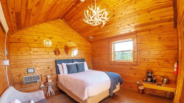 A cozy wooden cabin bedroom with a large bed, a small table, and a window.