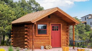 A small log cabin with a red door, a window, and a patio area with a table and chairs.